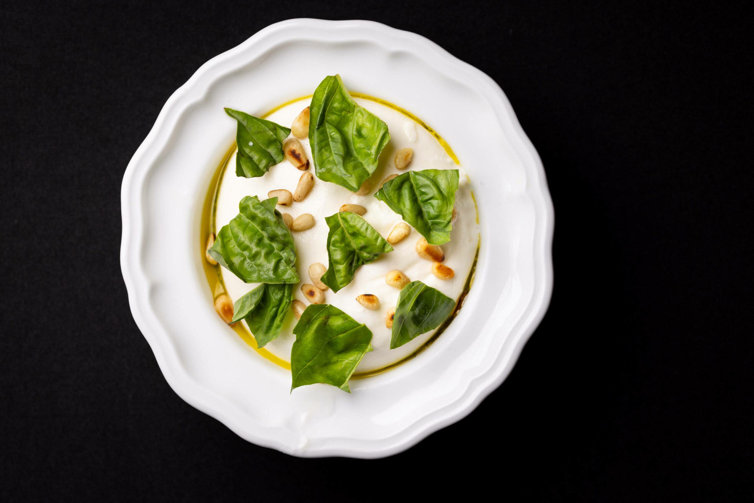 A creamy basil pesto dish garnished with fresh basil leaves and toasted pine nuts, presented in a classic white bowl.