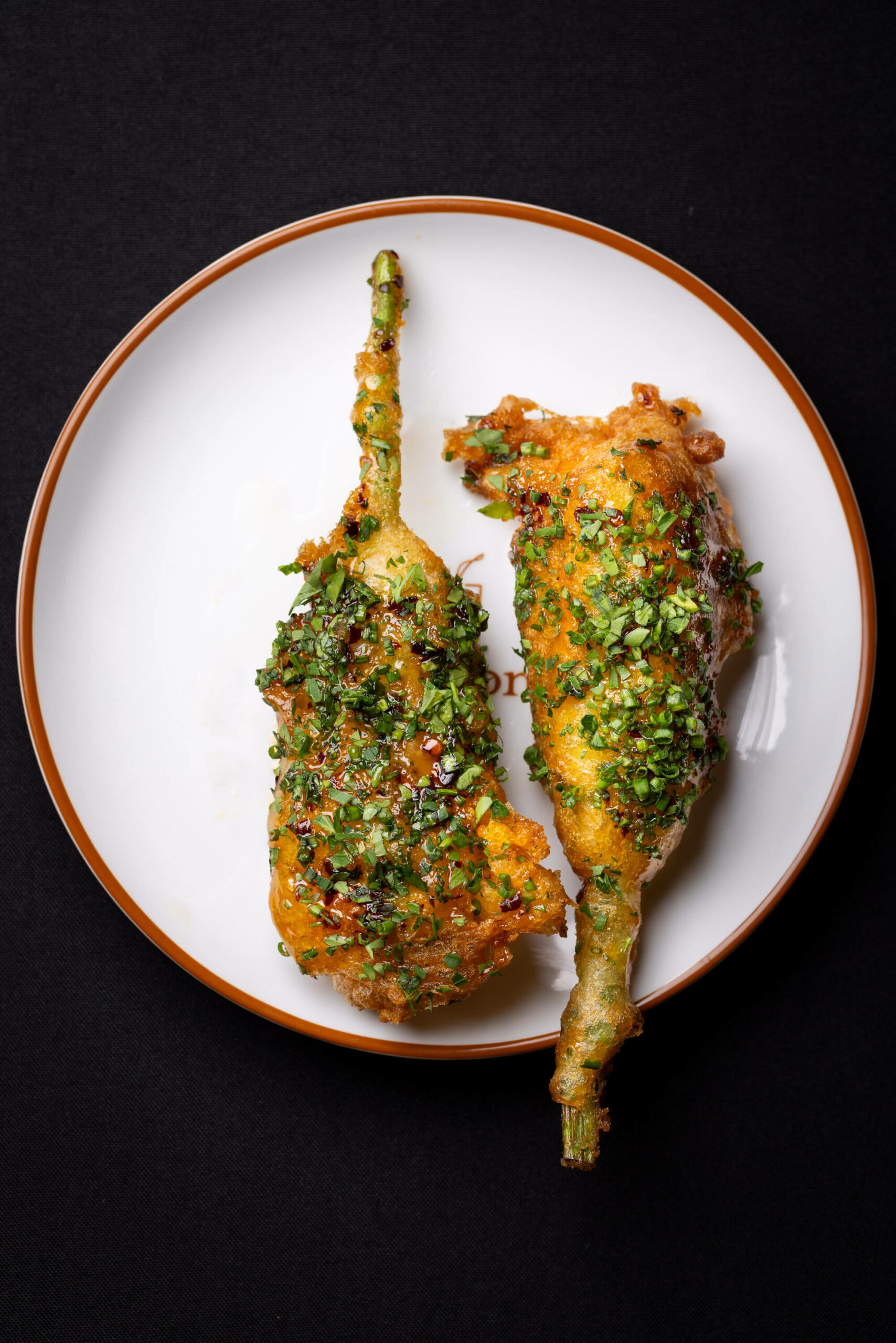 Crispy stuffed squash blossoms, garnished with fresh herbs, presented on a simple white plate.