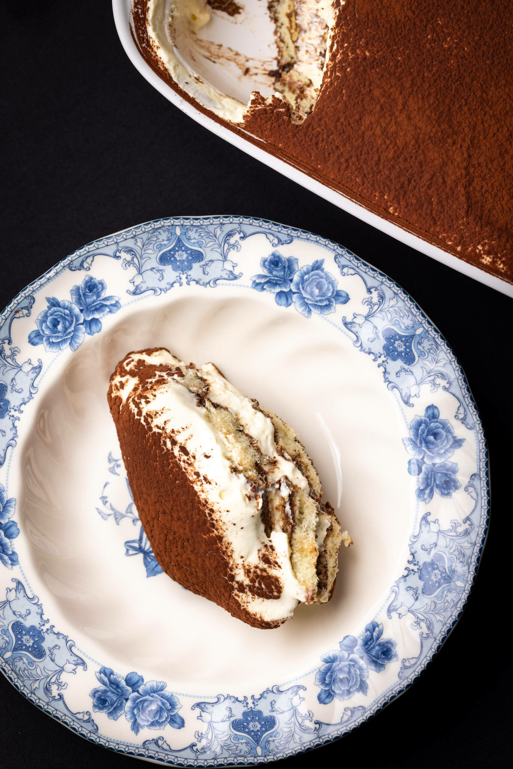 A portion of tiramisu served alongside the full tray, emphasizing its classic and elegant presentation.