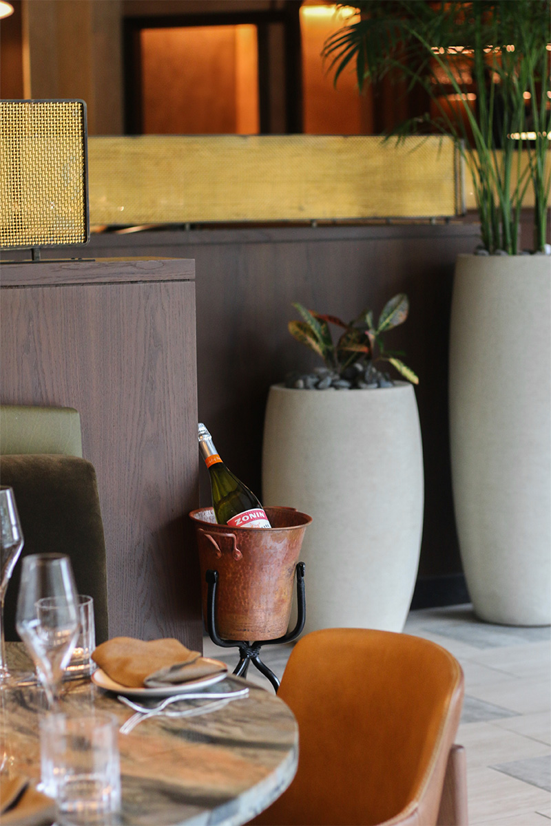 A bottle of Zonin Prosecco chilling in a rustic copper ice bucket beside a set dining table.