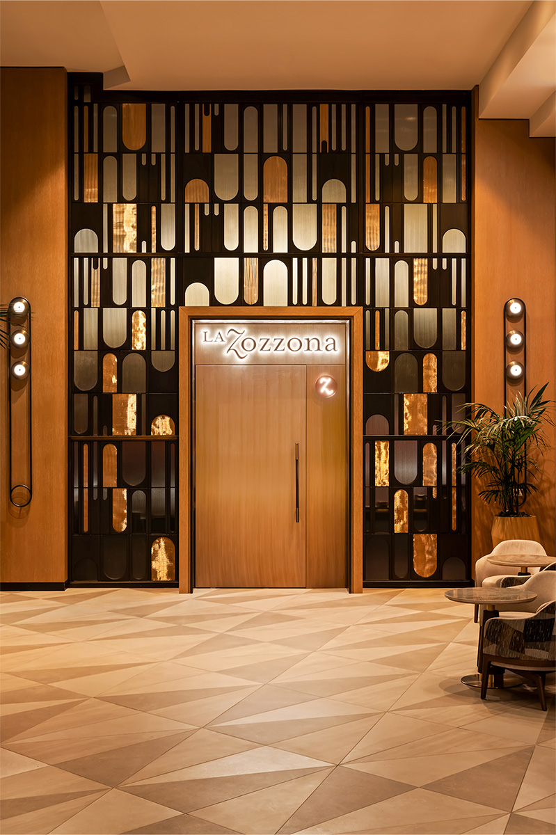 Elegant entrance to La Zozzona featuring geometric wall design and illuminated signage.