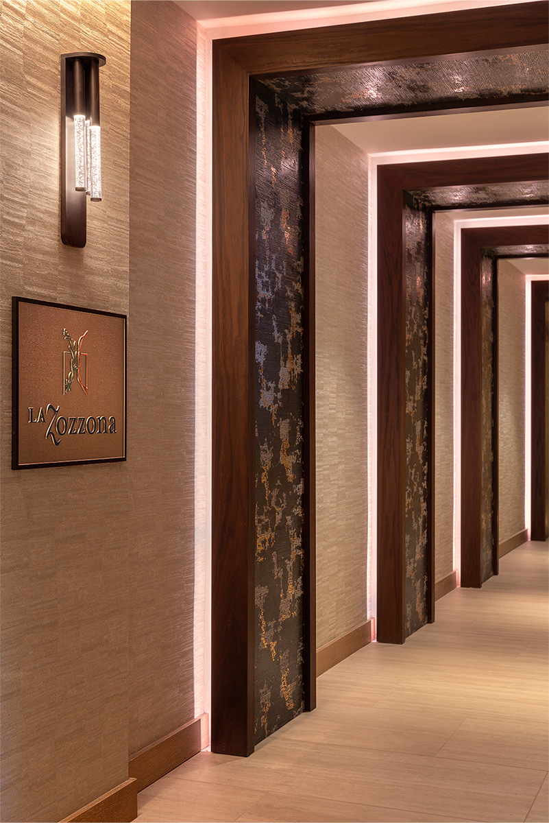 Warmly lit hallway with modern lighting and textured walls leading to La Zozzona.
