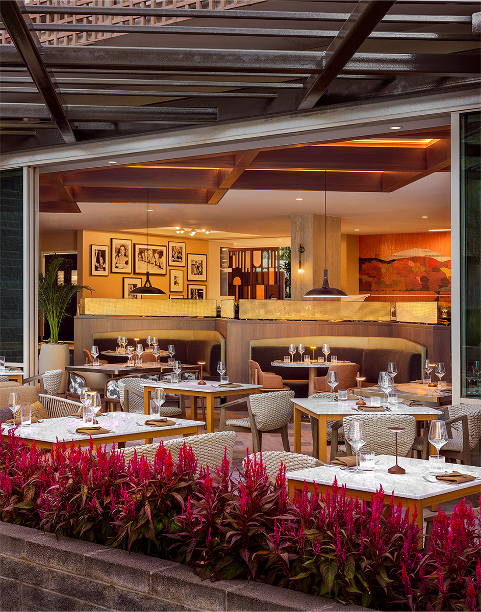 Chic outdoor dining area at La Zozzona with wicker chairs, white marble tables, and vibrant red flowers.