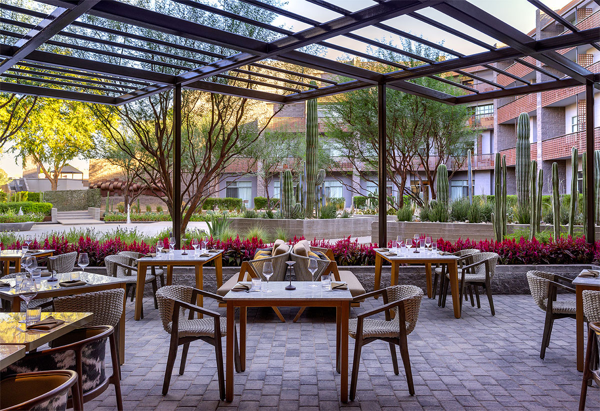 Outdoor patio seating at La Zozzona, surrounded by lush landscaping and cactus-lined gardens.
