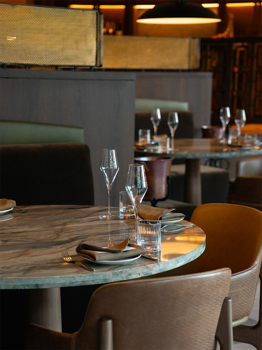Close-up of a marble table set for four with warm-toned chairs and golden napkins.