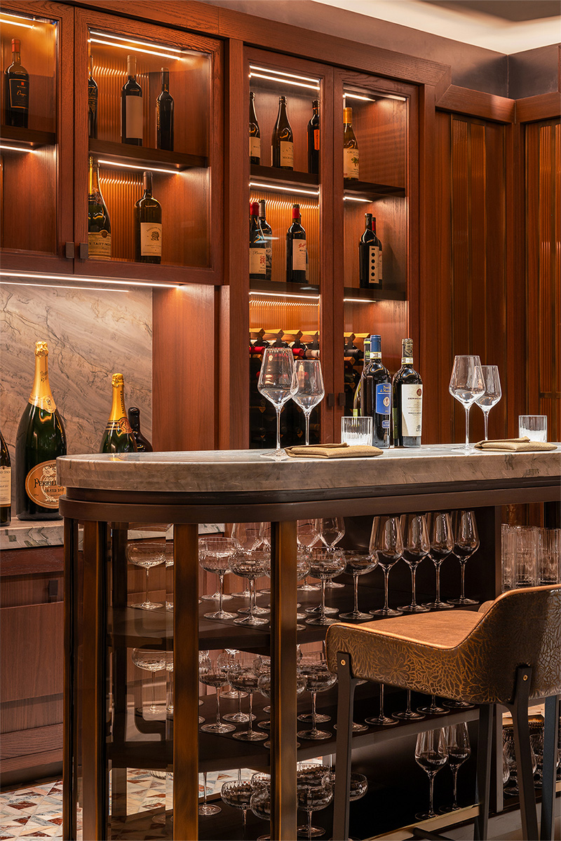 Stylish wine bar with illuminated bottle displays, elegant glassware, and a stone countertop.